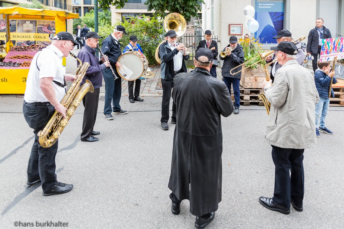 Auftritt der Band vom Swissjazzorama am Samstagsmarkt in Uster, organisiert von Herzkern. Eine Gruppe Männer steht im Kreis und spielt auf verschiedenen Instrumenten.